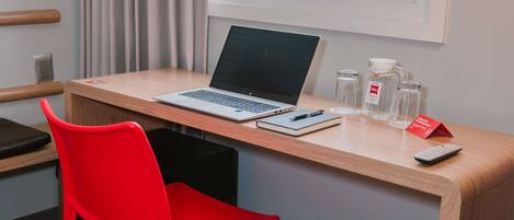Espacio de trabajo en un hotel con una computadora portátil, libreta, bolígrafo y control remoto sobre un escritorio de madera.