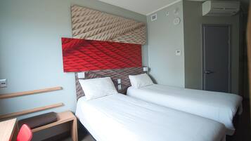 Ein Hotelzimmer mit zwei Betten, einem Schreibtisch, einem Stuhl und einer Wandklimaanlage.