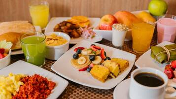 Un bufé de desayuno con diversos platos, como panqueques, huevos revueltos y fruta.