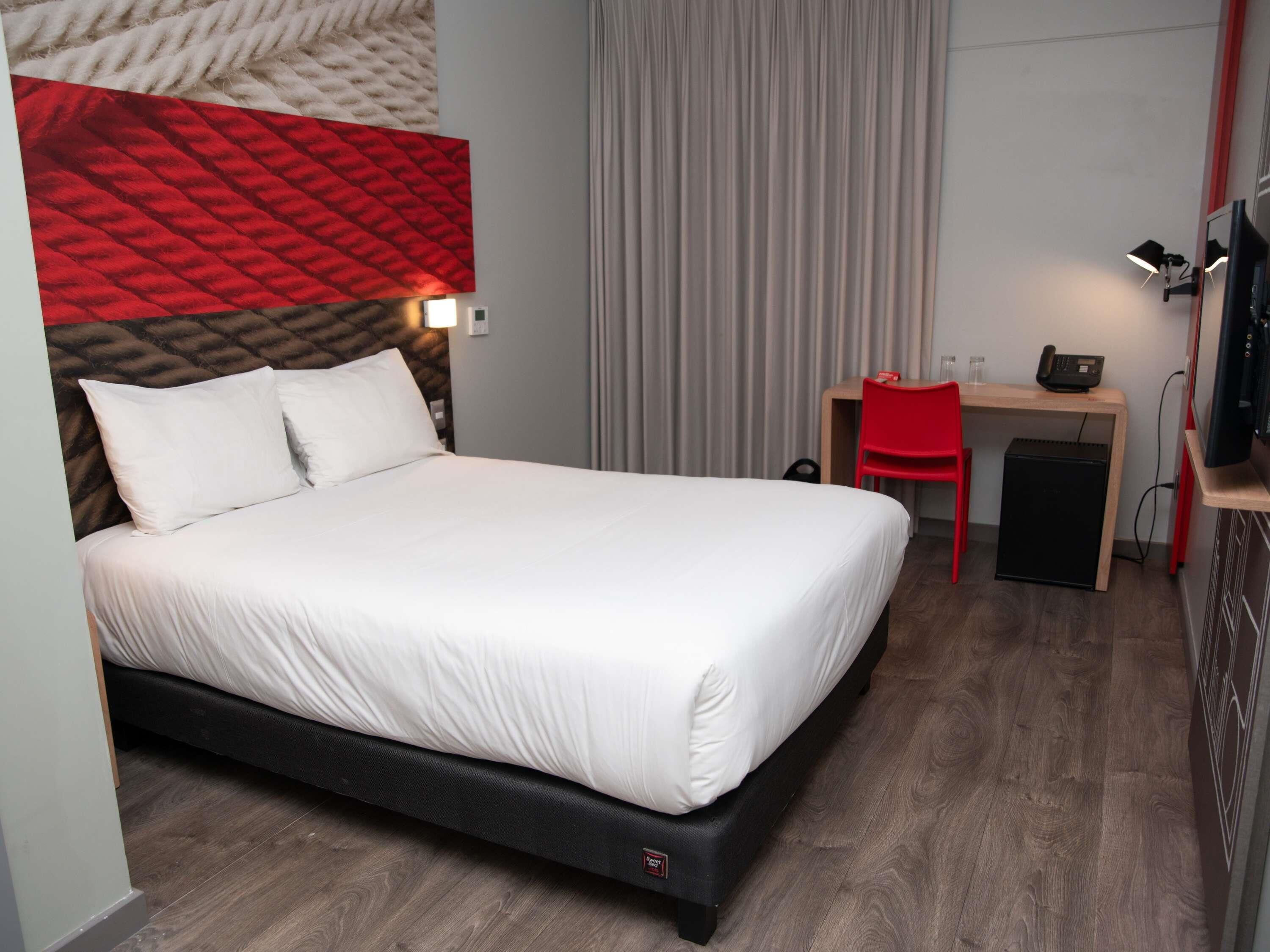 A hotel room with a bed, a desk with a chair, a television, and a small cabinet.
