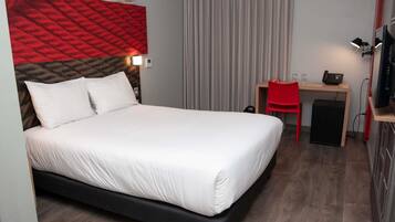 A hotel room with a bed, a desk with a chair, a television, and a small cabinet.