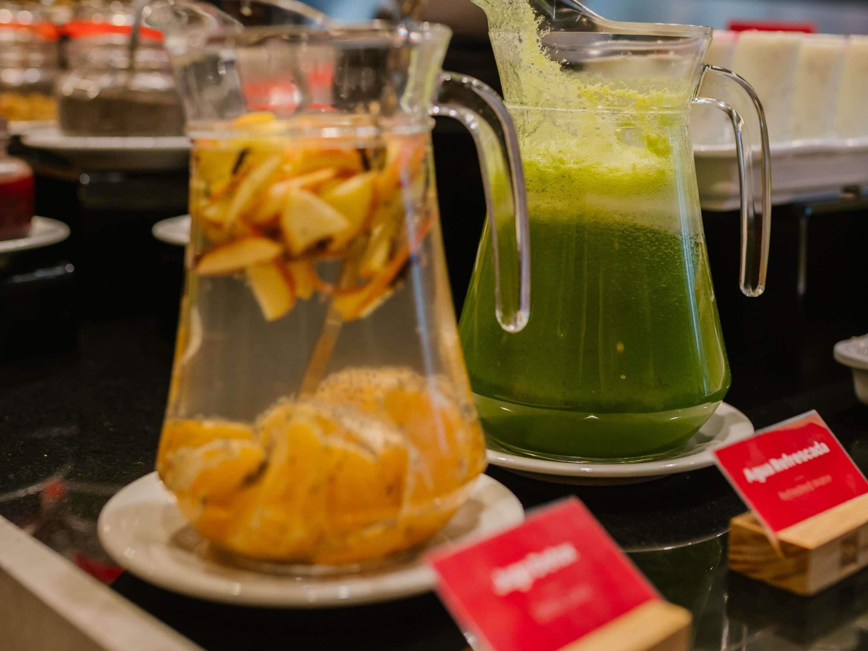 A beverage station with a pitcher of green juice and a glass container with sliced fruit.