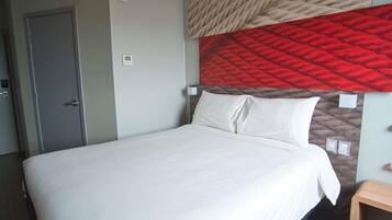 Una habitación de hotel con una cama grande, una mesita de noche de madera, un cabecero acolchado rojo y una puerta con manija.