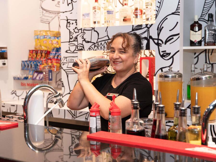 A person at a bar counter with a variety of bottles and a tap.