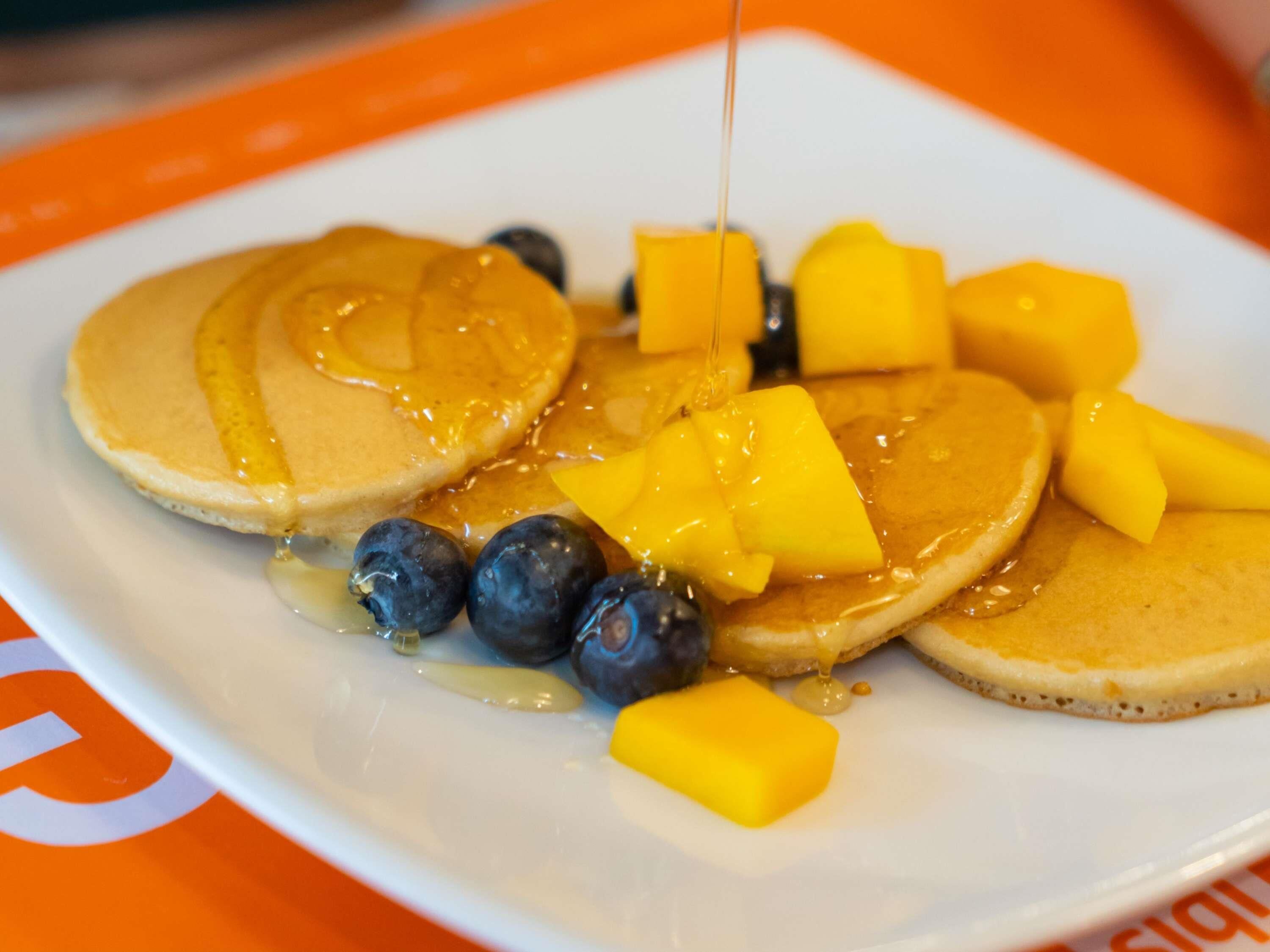 A plate of pancakes with syrup, blueberries, and mango chunks.