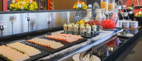 A buffet with various food items, including sliced meats, fruits, and beverages.