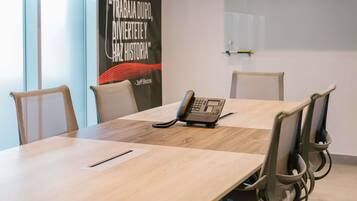 A conference room with a wooden table, chairs, a telephone, and a poster on the wall.