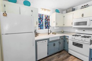 A kitchen with white appliances, blue cabinets, and a colorful window. - Aerobear Den • Fenced • Pup Friendly | LOCATION (Big Bear)