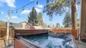 Un jacuzzi en un patio trasero con terraza de madera, rodeado de árboles y cerca de madera.
