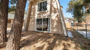 A two-story building with a large glass door entrance, surrounded by pine trees and a fenced yard.