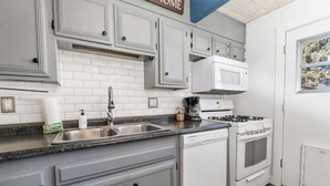 Una cocina con armarios blancos, un lavamanos de acero inoxidable, lavavajillas, estufa y microondas.