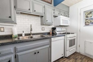 Una cocina con armarios blancos, un lavamanos de acero inoxidable, lavavajillas, estufa y microondas.
