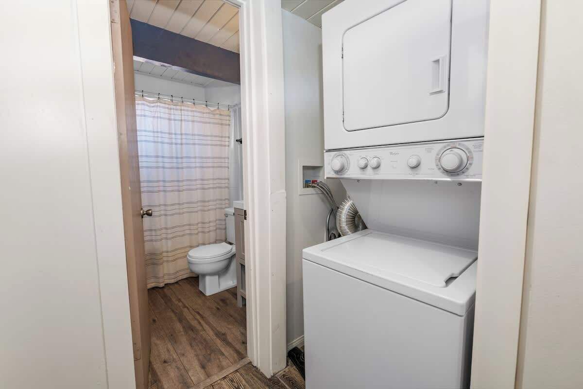 Une petite buanderie comprenant un lave-linge, un sèche-linge, des toilettes et un espace douche.