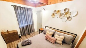 Une chambre à coucher comprenant un lit, une commode, une table de chevet, un miroir et des œuvres d’art décoratives au mur.