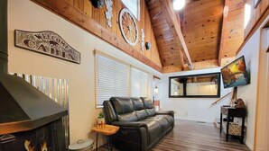 L’intérieur d’une cabane comprend une cheminée, un canapé en cuir, un plancher en bois et un téléviseur.