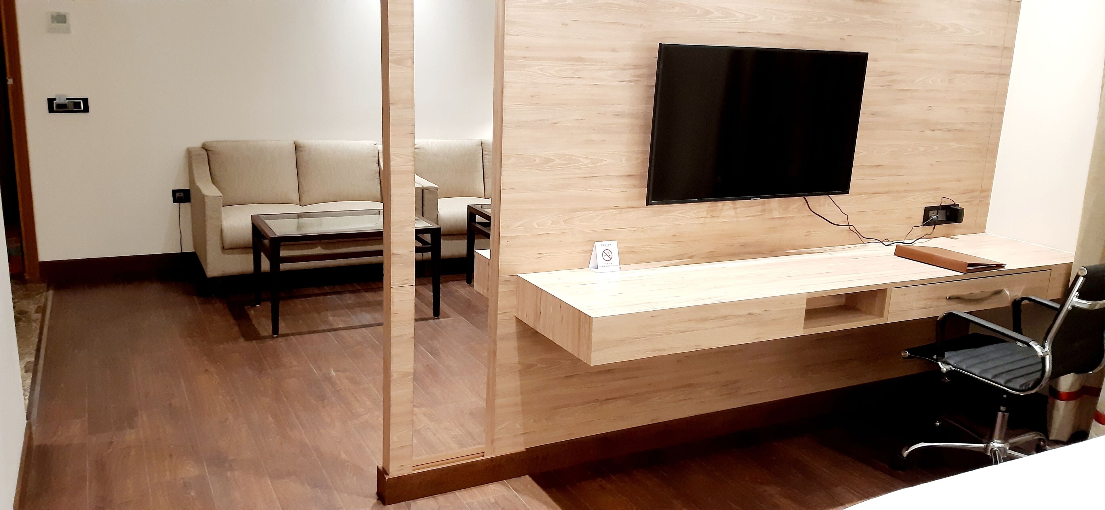 A modern living room with a sofa, a coffee table, a TV mounted on the wall, and a wooden desk with a chair.