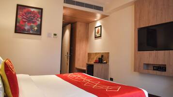 A hotel room with a bed, a TV mounted on the wall, a wooden wardrobe, and a framed picture on the wall.