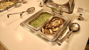A buffet with labeled containers of potato wedges and green peas.