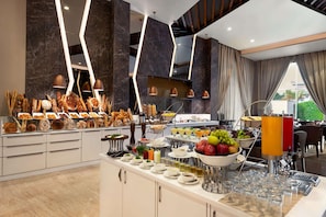 A buffet area with various food items and beverages, modern lighting fixtures, and a view of the outdoors.