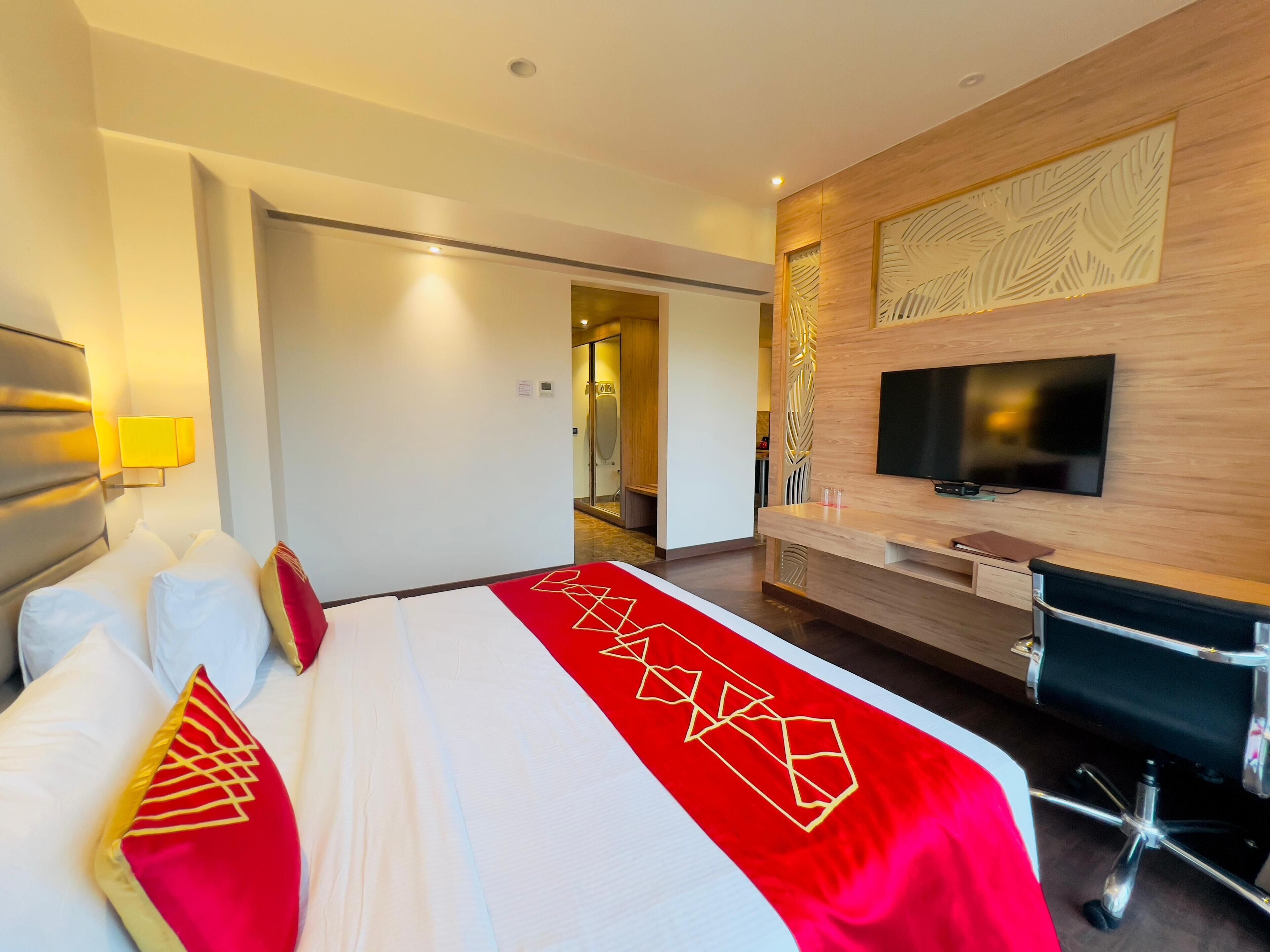 A hotel room with a large bed, a TV, a desk, and a bathroom visible through an open door.