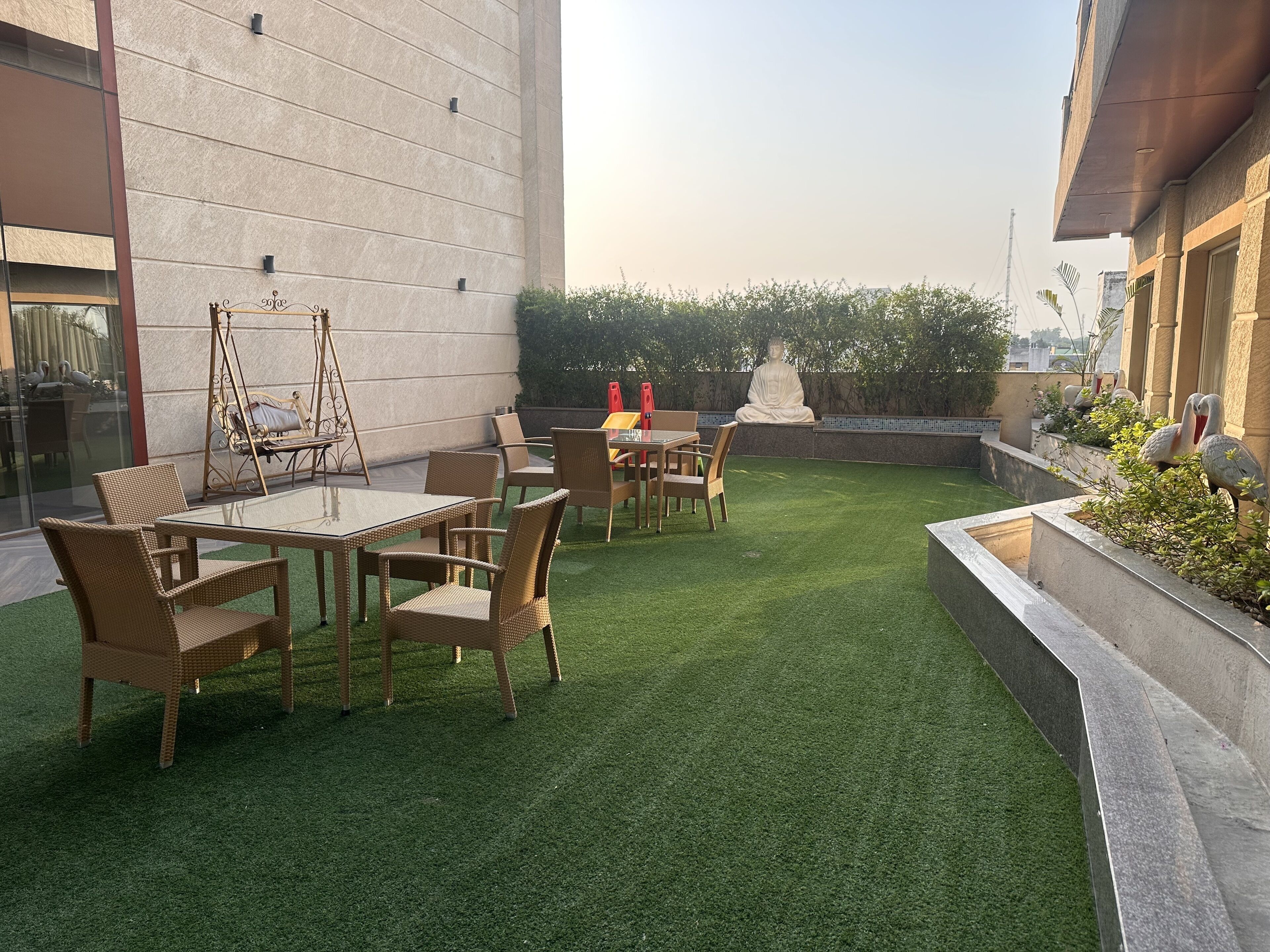A rooftop garden with a dining area, a swing chair, and a statue.