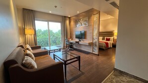 Une chambre d’hôtel moderne dotée d’un canapé, d’une table basse, d’une télévision et d’un balcon offrant une vue sur les arbres.