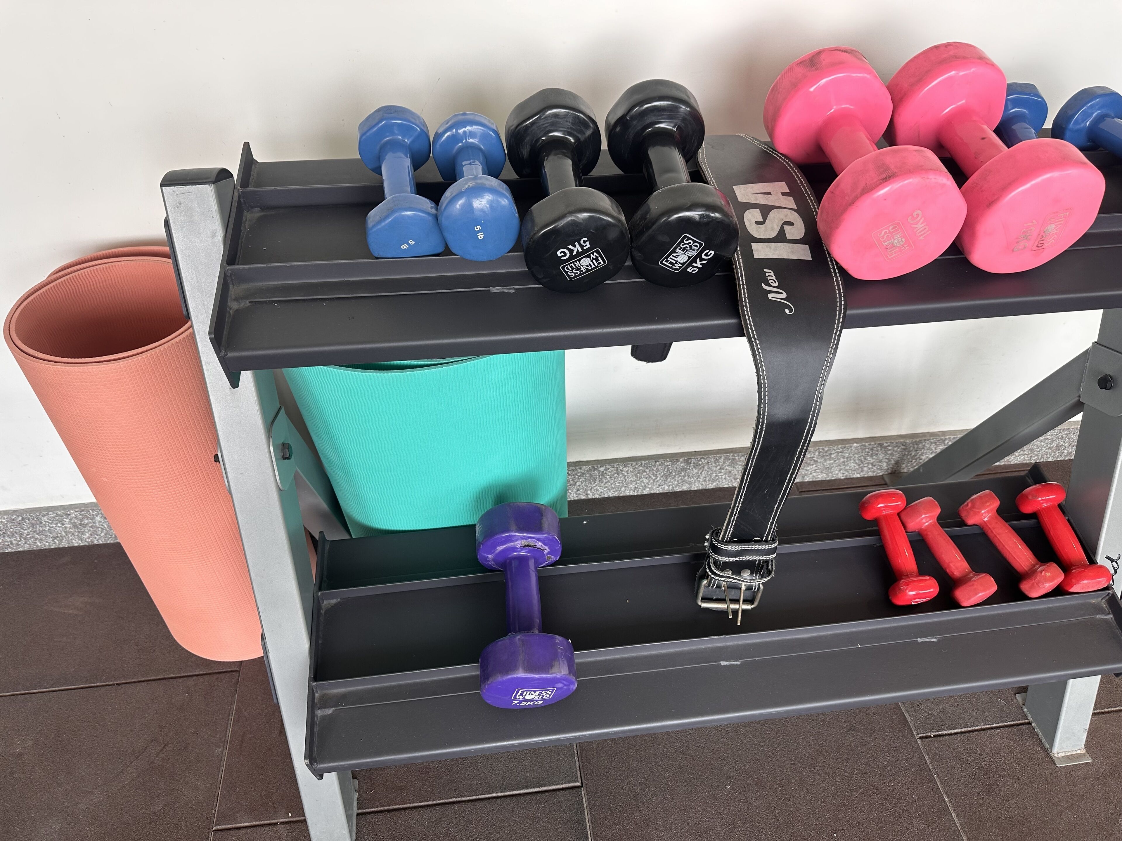 A weightlifting bench with various dumbbells and a trash can.