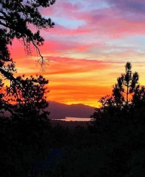 Une vue au coucher du soleil, avec des montagnes en arrière-plan et des arbres au premier plan.