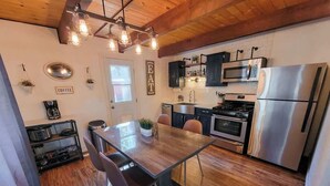 A modern kitchen with a wooden dining table, stainless steel appliances, and a hanging light fixture.