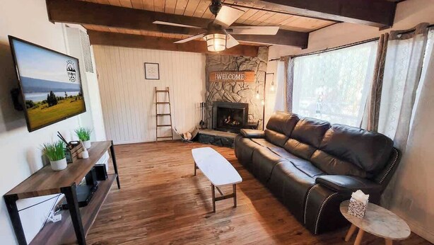 A cozy living room with a wooden floor, a leather sofa, a coffee table, a TV mounted on the wall, and a fireplace.