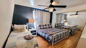 A room with two metal bunk beds, a small bedside table with a lamp, a mirror, and a ceiling fan.