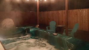 A hot tub area with a wooden fence, string lights, and two green chairs.