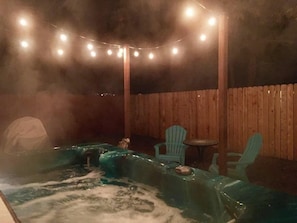 Ein Bereich mit Whirlpool, Holzzaun, Lichterkette und zwei grünen Stühlen.