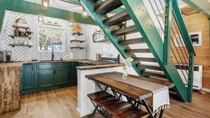 A kitchen with a herringbone tile backsplash, wooden cabinets, a central island, and a green staircase.