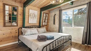 A wooden-paneled room with a bed, a window with curtains, and a view of the outdoors.