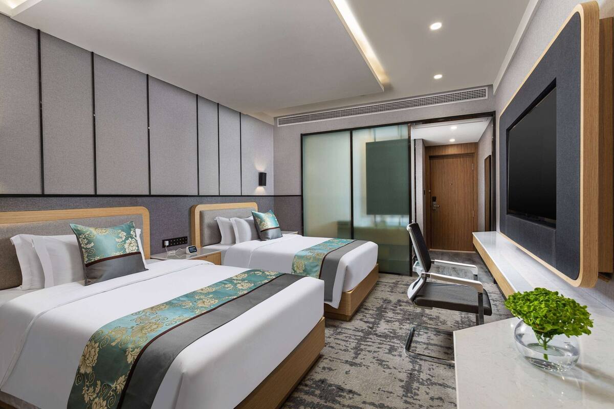 A hotel room with two beds, a TV, a desk, and a chair.