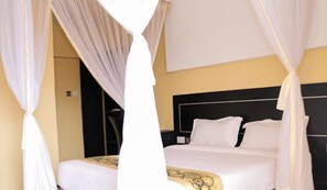A bed with white bedding and a black headboard, surrounded by white curtains. - Anchor Hotel (Nairobi)