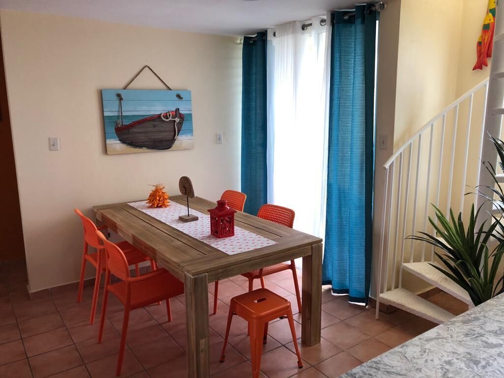 A dining area with a wooden table, orange chairs, a red lantern, and a wall-mounted painting of a boat.