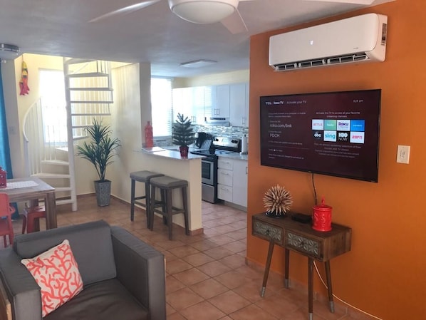 A living room with a sofa, a coffee table, and a TV mounted on the wall displaying a Roku interface.