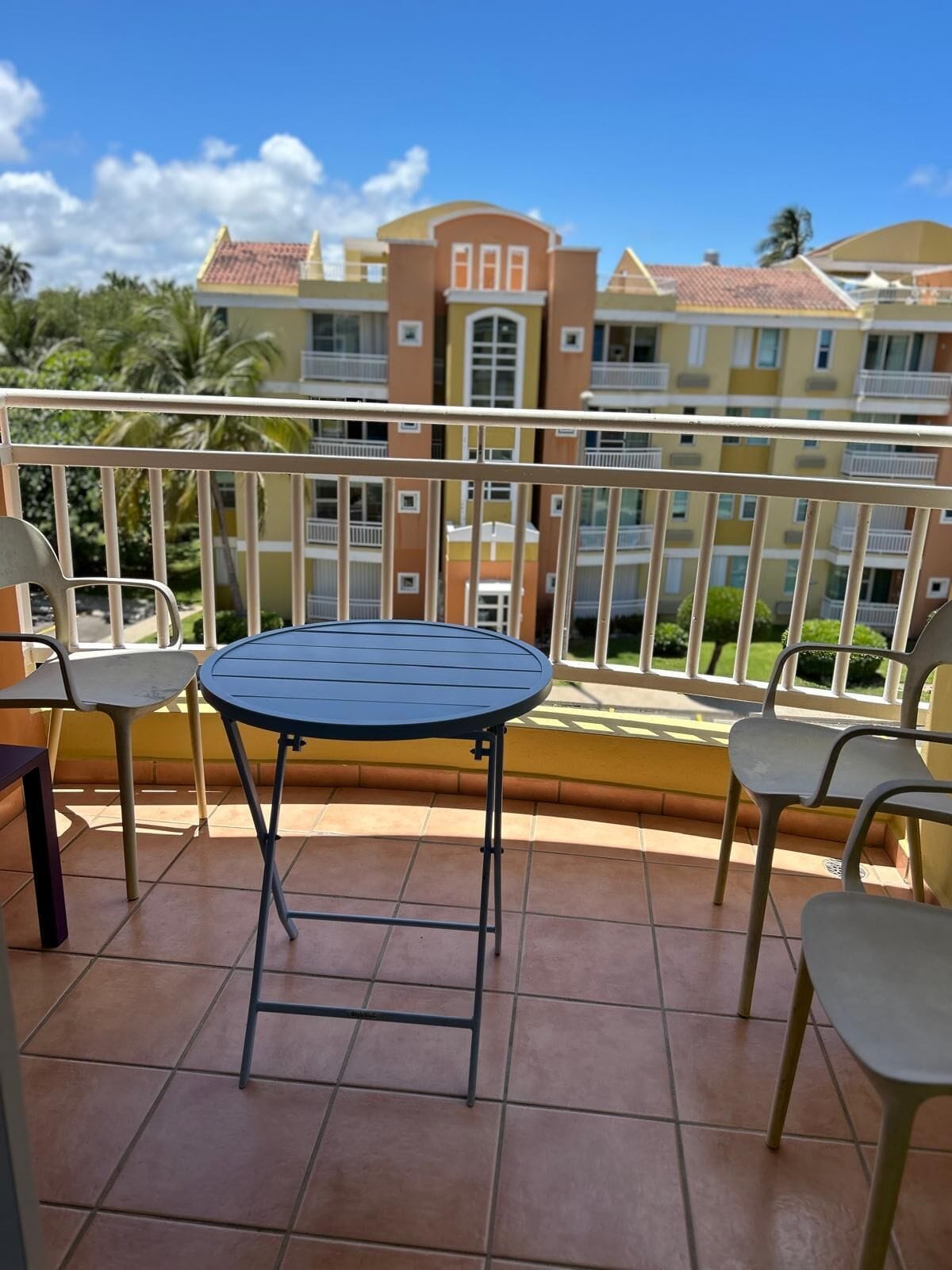 A balcony with a round table and four chairs, overlooking a residential building with balconies.