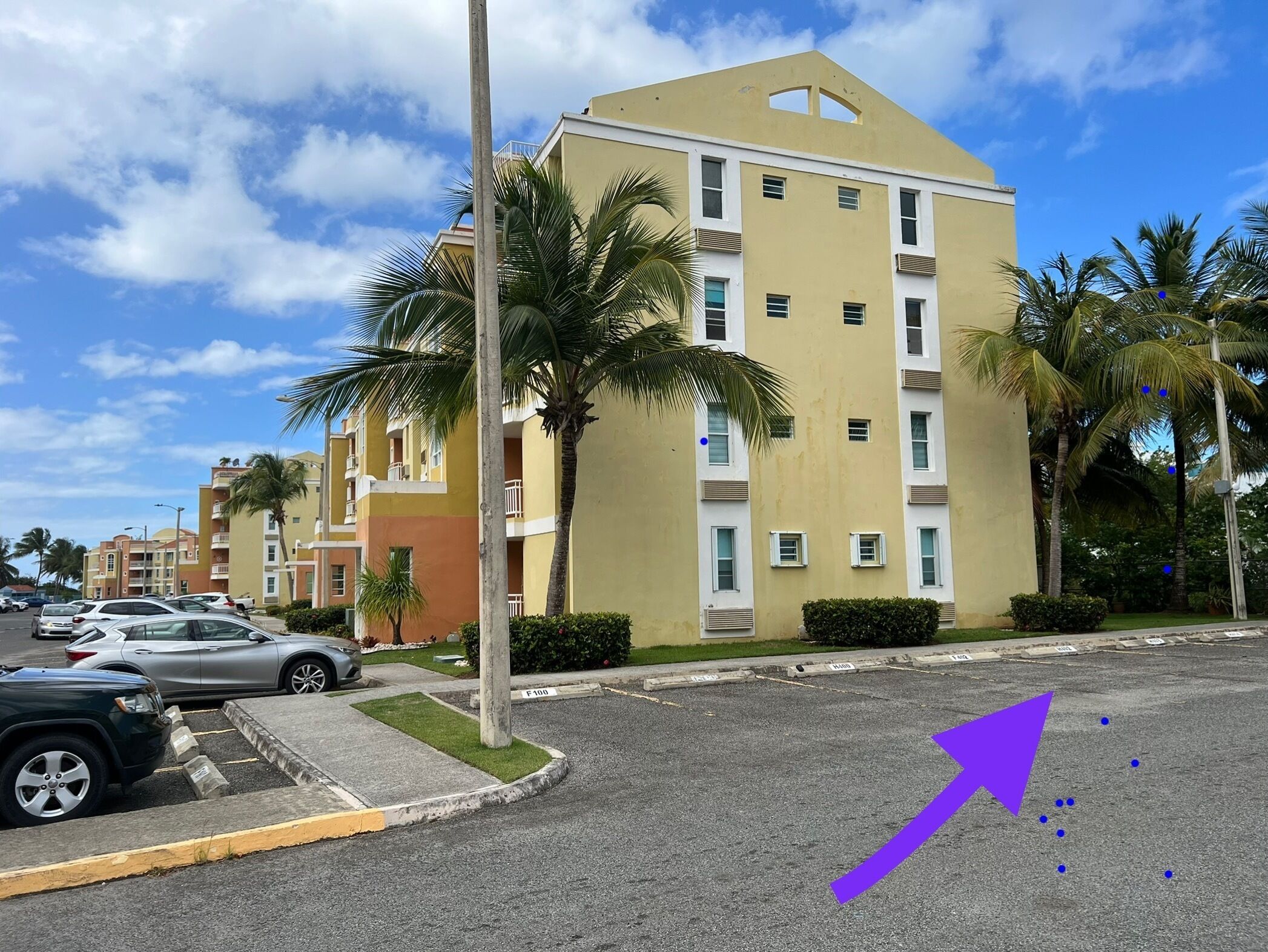 A multi-story hotel with a yellow facade, palm trees, and a parking lot.