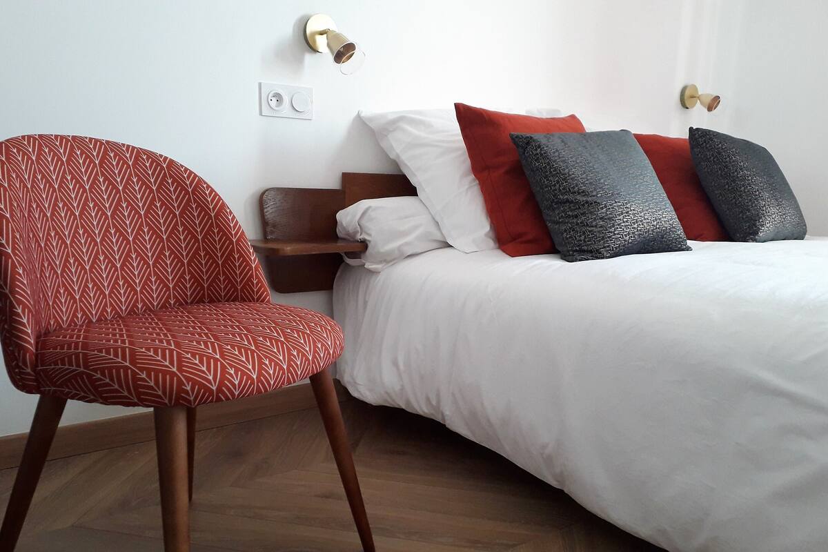 Une chambre d’hôtel avec un lit, une chaise et une prise de courant au mur.