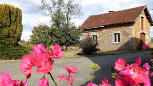 Un bâtiment en pierre, doté d’un toit en tuiles, entouré de verdure et de plantes en fleurs.