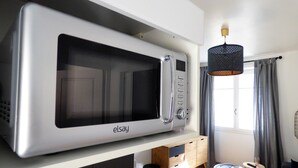 Une cuisine moderne avec un grand four à micro-ondes argenté, un meuble en bois, une petite table ronde avec une chaise et un luminaire suspendu.