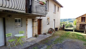 Un bâtiment à deux étages doté d’un balcon, d’un petit espace extérieur aménagé avec deux chaises et une table, et offrant une vue sur la campagne.