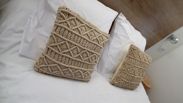 Un lit avec deux coussins en macramé de couleur beige et des draps blancs.
