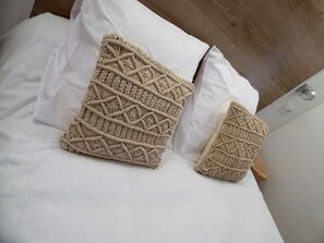 Un lit avec deux coussins en macramé de couleur beige et des draps blancs.