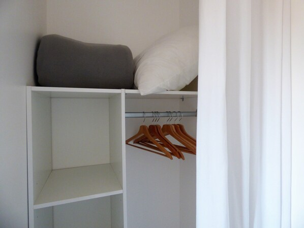 Un vestidor amplio con una cama en la parte superior, una barra para colgar ropa con perchas de madera y varios estantes.