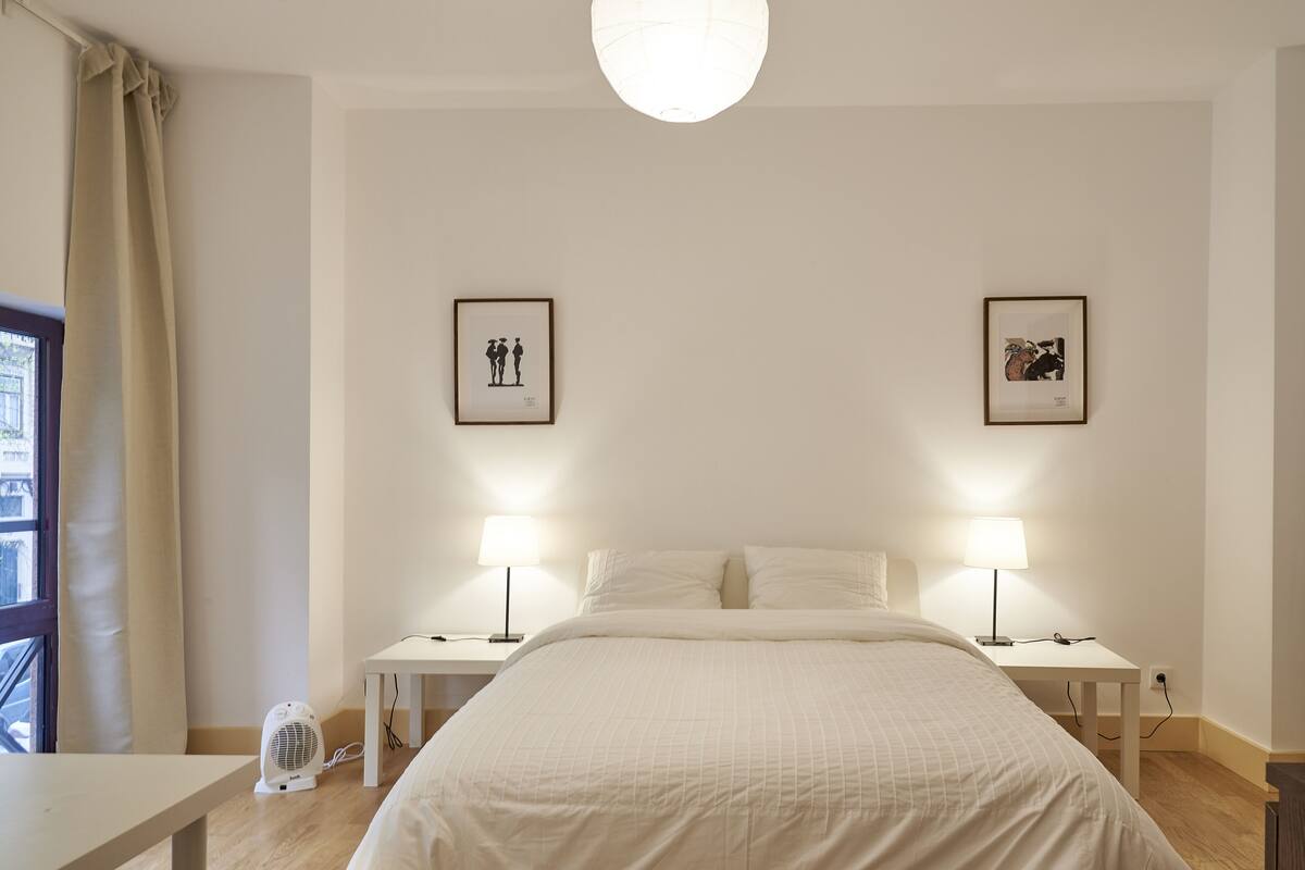 Een keurig opgemaakt slaapkamer met een groot bed, twee nachtkastjes met lampen en twee ingelijste foto’s aan de muur.