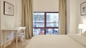 A hotel room with a bed, a desk with a chair, a window with curtains, and a wall-mounted lamp. - Campo Pequeno Avenida (Lisbon)